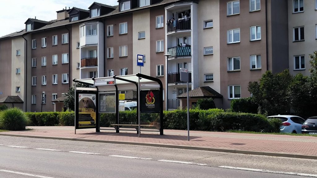 Przystanek autobusowy przy ulicy na osiedlu z widocznymi w tle blokami mieszkalnymi